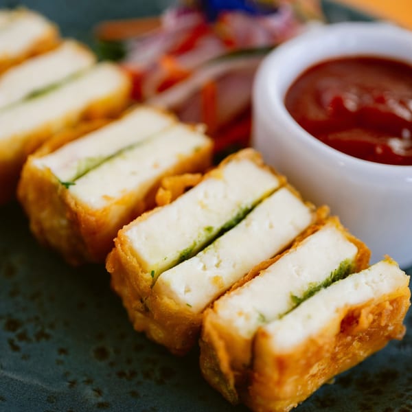 Golden-fried paneer pakora with green chutney filling, served with a side of red dipping sauce.