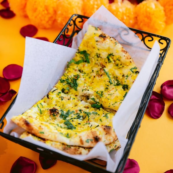 Indian garlic naan bread, garnished with cilantro, in a black basket on a yellow surface with rose petals.