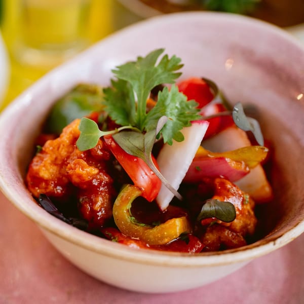 Close-up of Saffron's Indian dish with chicken, bell peppers, and cilantro in a pink bowl.