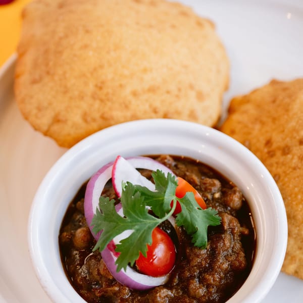 Saffron's Chole Bhature, with a bowl of chickpea curry garnished with onion, tomato, and cilantro.