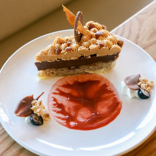 A slice of Indian chocolate tart with caramel frosting, strawberry sauce, and berry garnish.