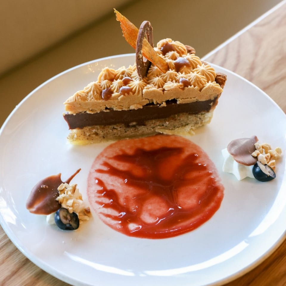 A slice of Indian chocolate tart with caramel frosting, strawberry sauce, and berry garnish.