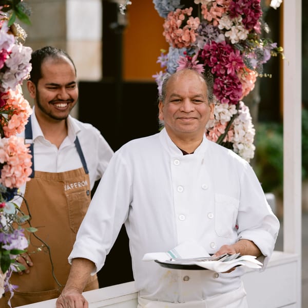 Two Saffron chefs, one smiling and holding a tray of silverware, surrounded by floral decorations.