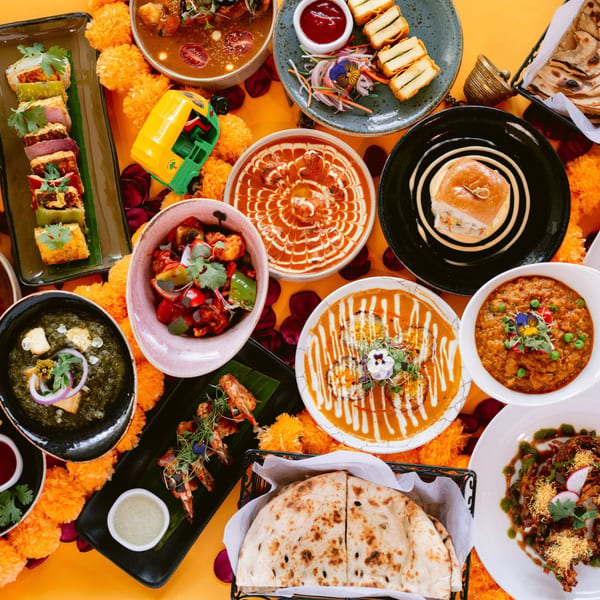A vibrant spread of Indian dishes, including curries, naan, and appetizers, on a yellow table.