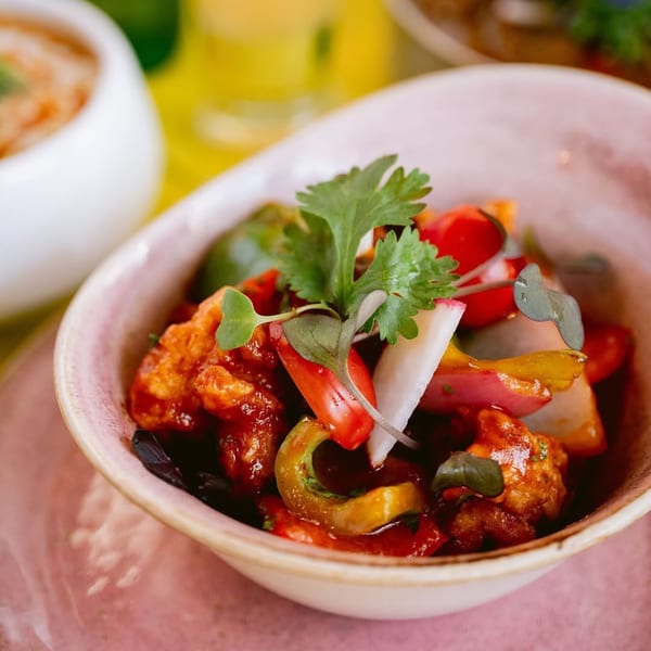 Close-up of a pink bowl filled with Indian chili chicken, bell peppers, and cilantro.