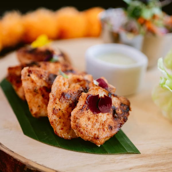 Grilled Indian chicken tikka pieces, garnished with edible flowers, served on a banana leaf.