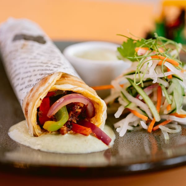 Saffron's Indian kathi roll, filled with vegetables and meat, served with a side salad and sauce.