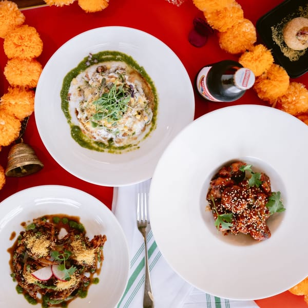 Three Indian dishes, including chaat and a sesame chicken dish, on a red table with marigold garlands.