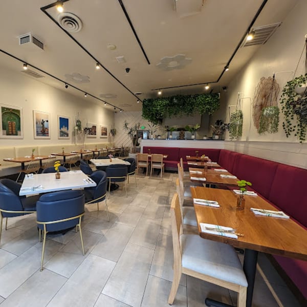 Saffron Indian restaurant interior with modern tables, blue and wooden chairs, red banquettes, and wall art.