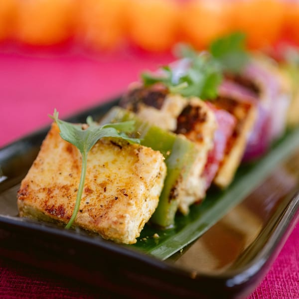 Indian paneer tikka with bell peppers and onions on a dark plate with a pink background.