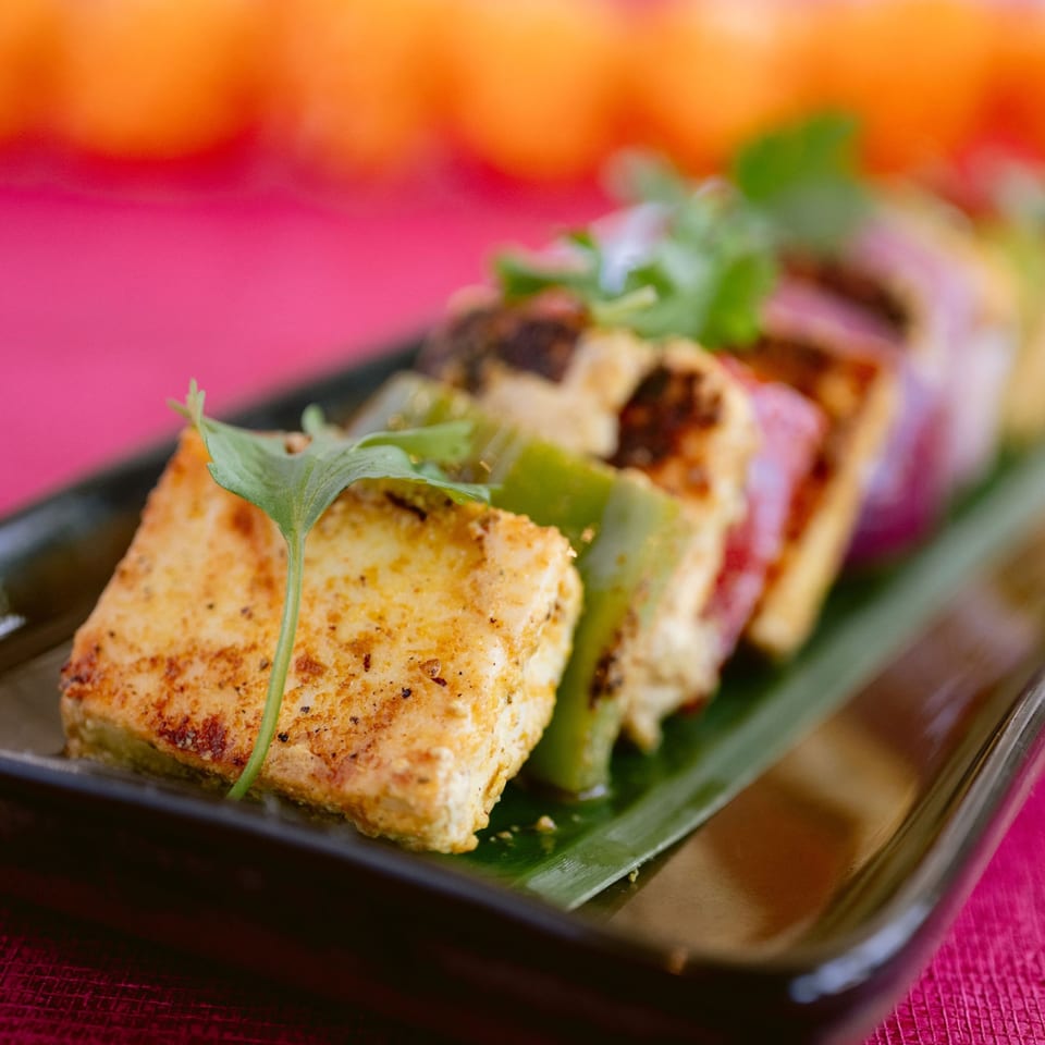 Indian paneer tikka with bell peppers and onions on a dark plate with a pink background.