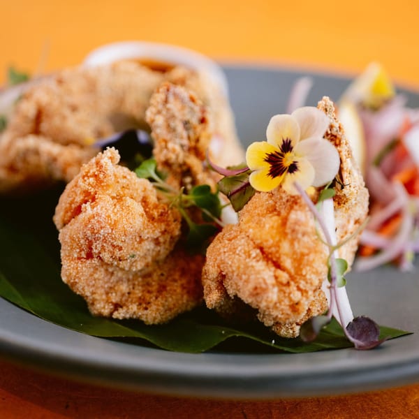 Crispy fried Indian appetizer, possibly chicken or paneer, garnished with an edible flower and microgreens.