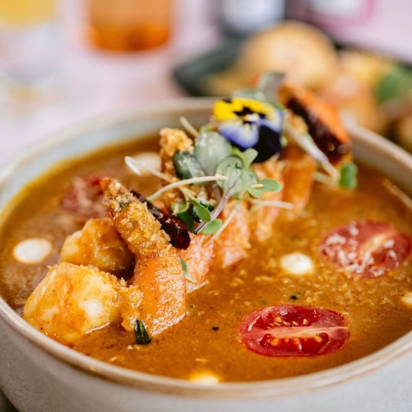 Saffron's Indian shrimp curry with cherry tomatoes, microgreens, and edible flowers in a bowl.