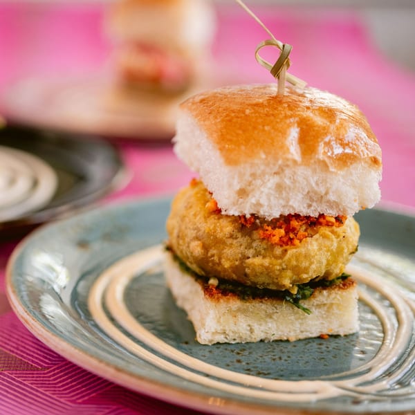 A Saffron vada pav, an Indian potato fritter slider, on a blue plate with a pink background.
