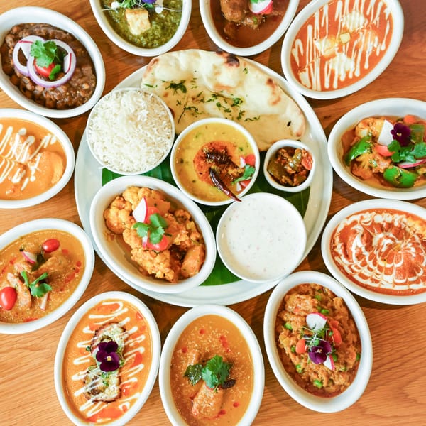 A vibrant spread of Indian dishes, including curries, rice, naan, and raita, on a wooden table.