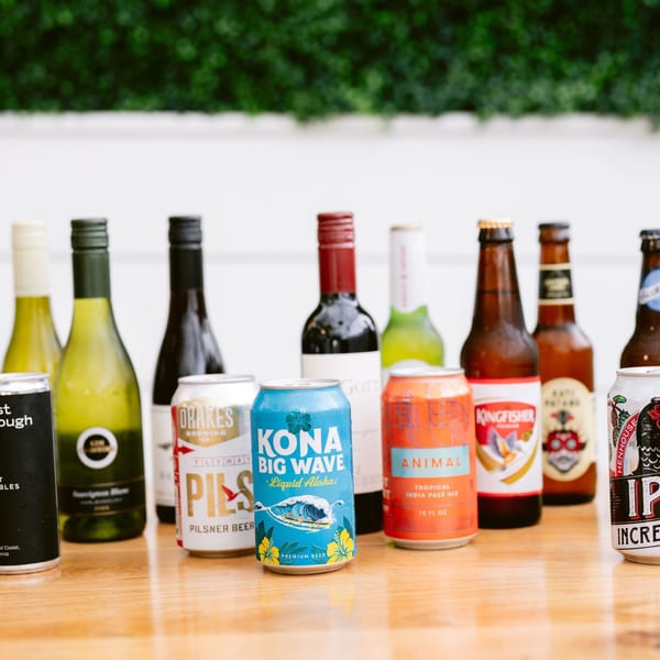 Assortment of wine bottles and beer cans, including Kingfisher, on a wooden table.