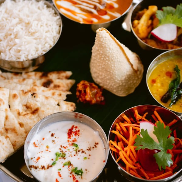 A close-up of an Indian thali with rice, naan, curries, raita, salad, and papadum.