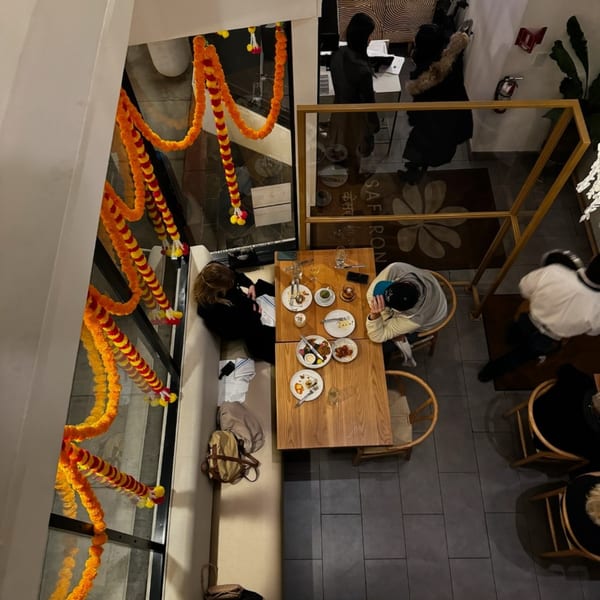Overhead view of Saffron Indian restaurant with diners, marigold garlands, and empty plates on wooden tables.