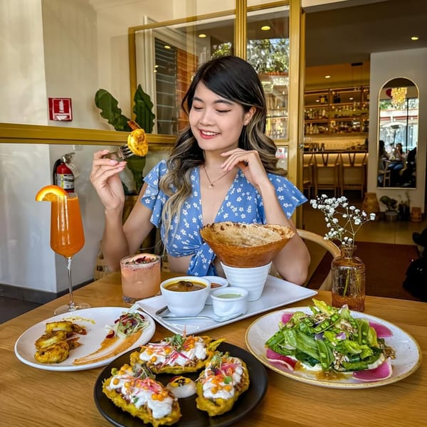 A smiling woman enjoying Indian food and drinks at Saffron, with a dosa, curry, and salad.