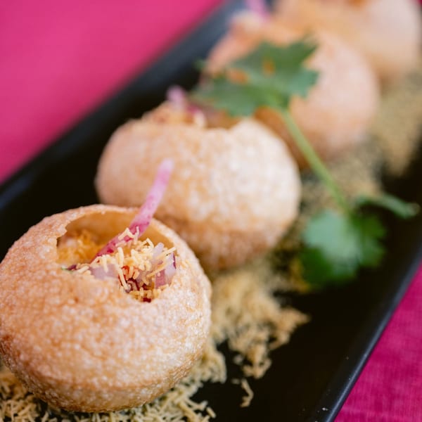 Four Indian pani puri, filled with spices and onions, garnished with cilantro on a black plate.