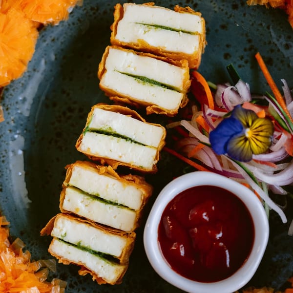Saffron's fried paneer with green chutney filling, served with a side of red sauce and salad.