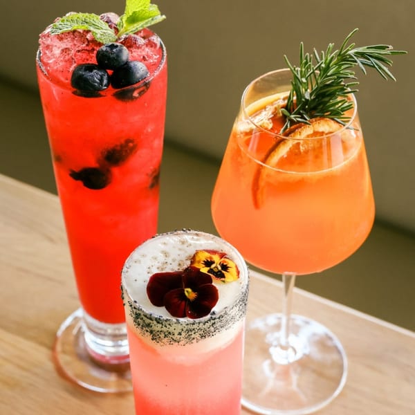 Three colorful Saffron cocktails: a red berry drink, an orange spritz, and a pink floral cocktail.