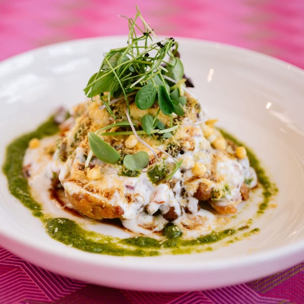 Indian chaat dish with yogurt, green chutney, and microgreens on a white plate.